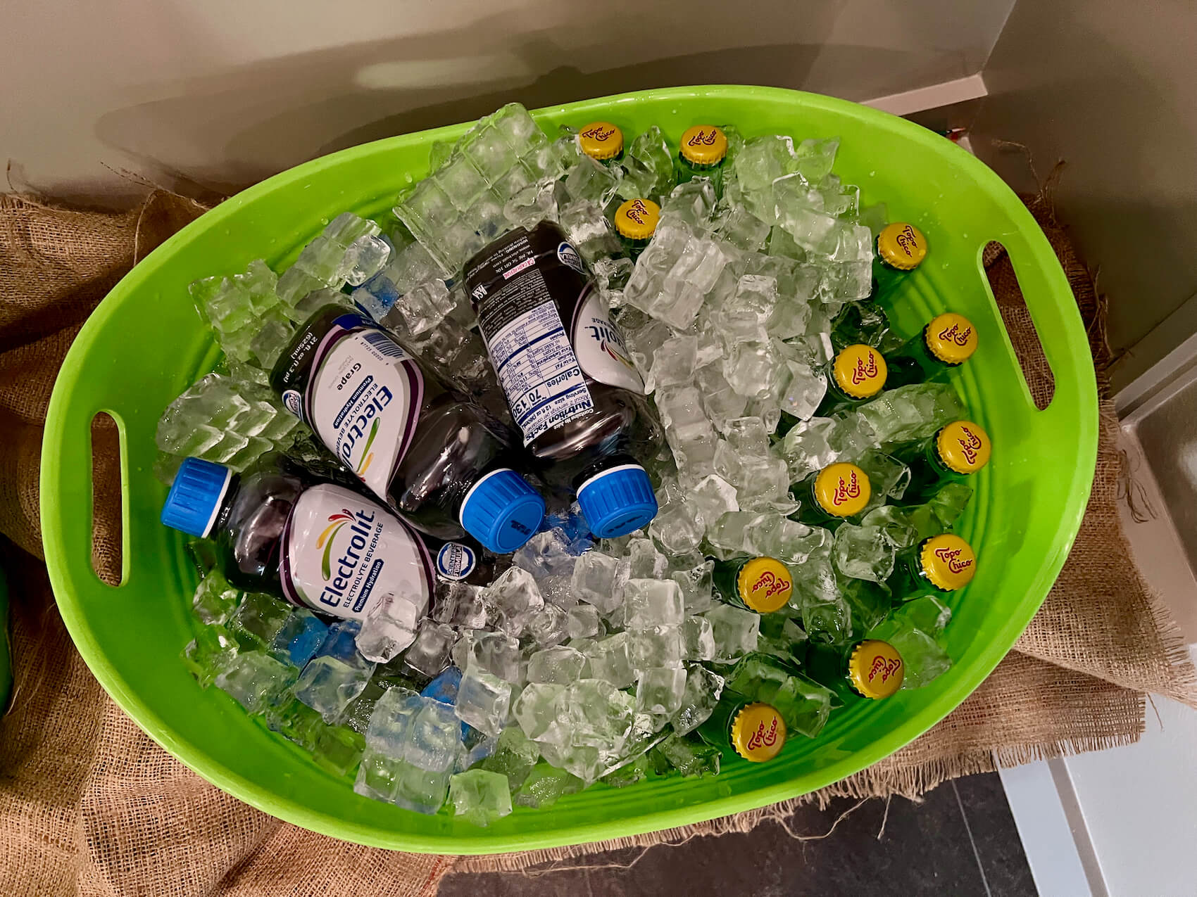 Green plastic bucket of Electrolit and Topo Chico full of ice