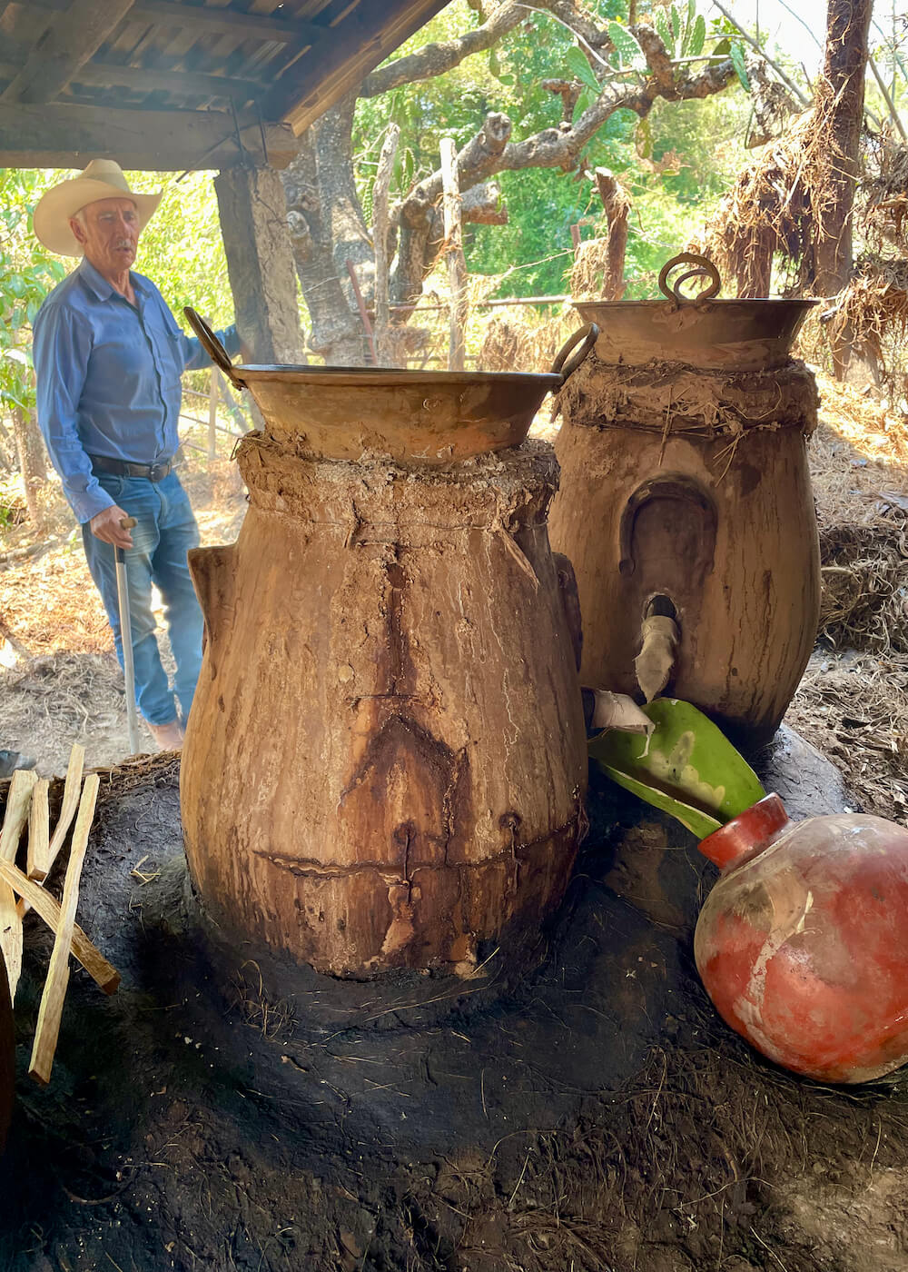 Don Luis stands behind two clay pot stills