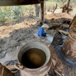 Don Luis feeds fire under small clay pot stills