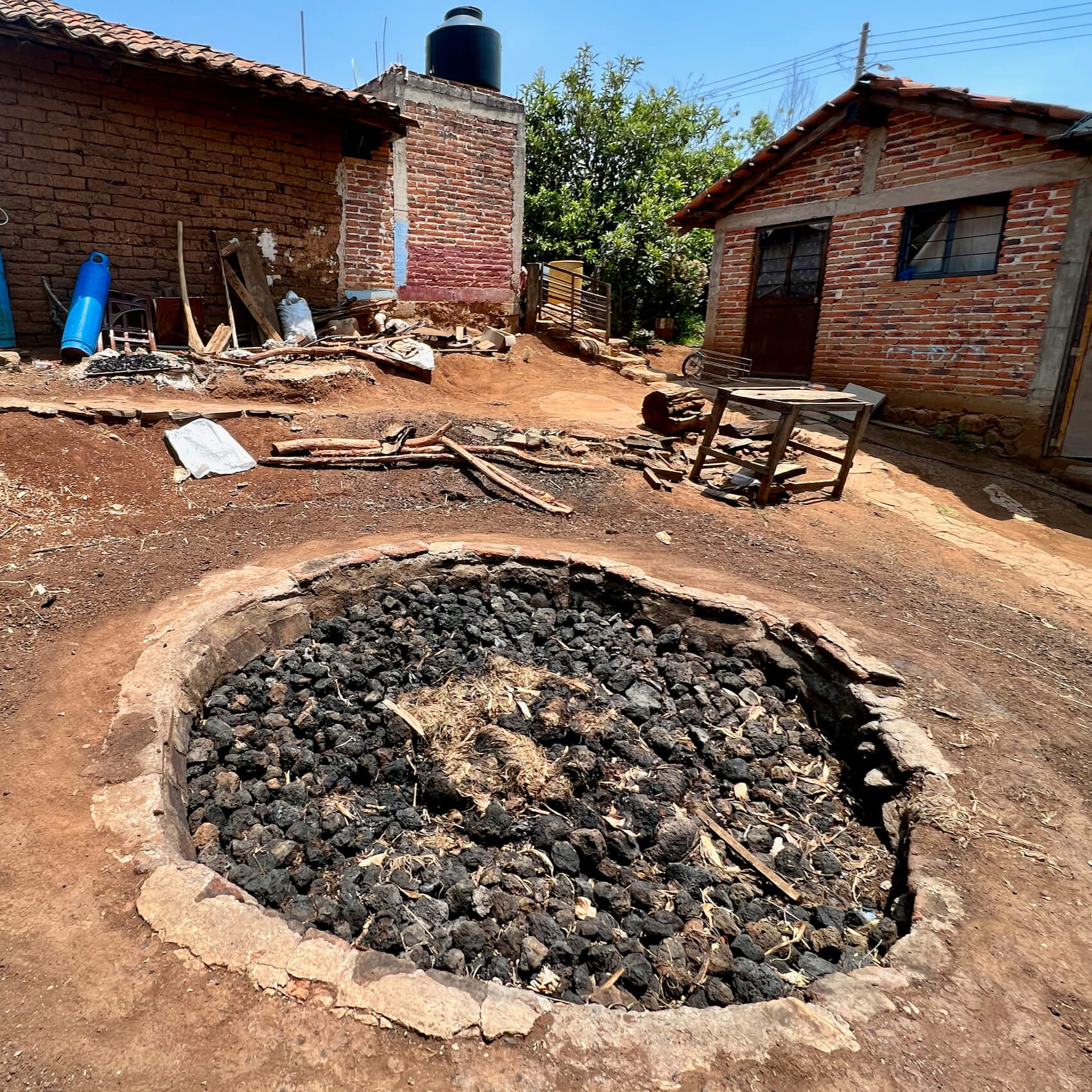 A large round pit filled with black volcanic rock for cooking agave